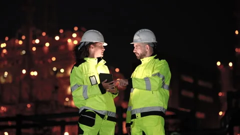 Female refinery engineer discusses tablet data with technician near illuminated Stock Footage 341479046