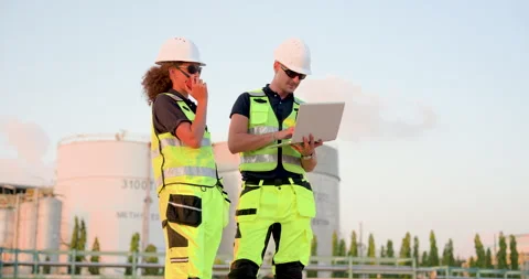 Female refinery technician speaking through walkietalkie while engineer reviews Stock Footage 338424180