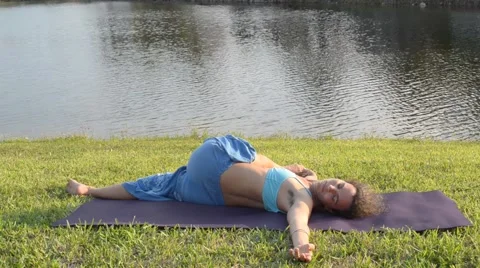Female releasing lowerback doing hips oppening outdoors near lake of residences 스톡 동영상 63497100