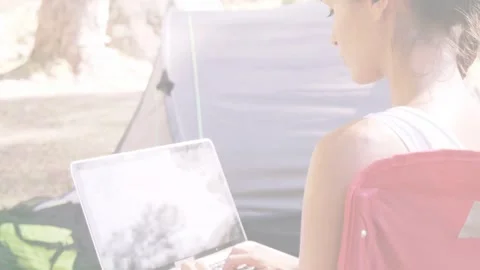 Female remote worker typing on laptop in red camping chair at campsite, noticing Stock Footage 333610271