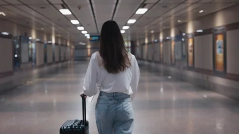 Female with rolling suitcase walks along passenger tunnel at railroad station Stock Footage 308033247