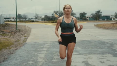 Female runner approaching camera on empty road with distant hills on horizon Stock Footage 339623188