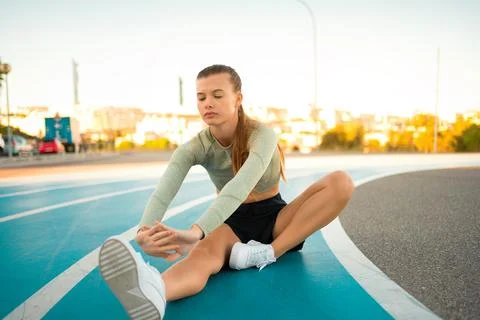 Female runner doing stretching exercises sitting on running track Stock-Fotos