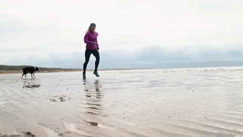 Female runner jogging on the beach with her dog in slow motion Stock Footage 113005474