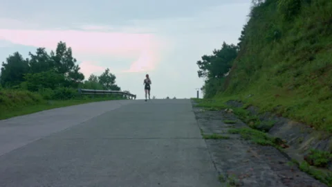 Female runner jogging uphill along a paved mountain road during sunset Stock Footage 342933952