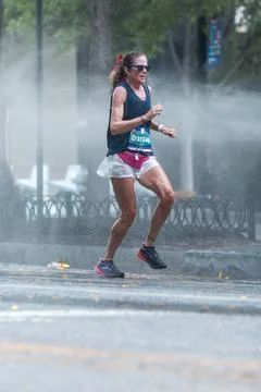 Female runner jogs through cooling spray at Atlanta 10K race Stock Photos