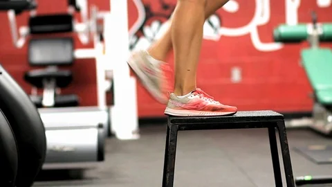 Female runner performing step ups on a plyo box holding weights in her hands Video stock 118027415