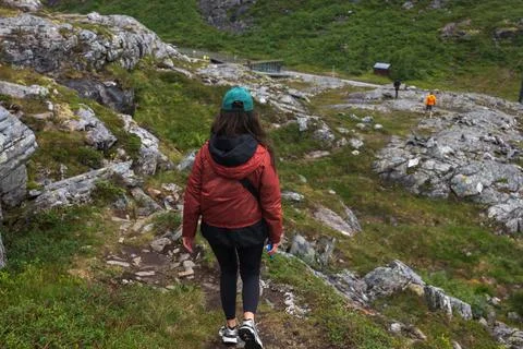 Female runner in red jacket ascending rocky mountain trail with moss-covered  Stock Photos