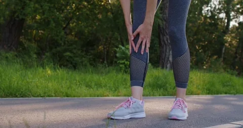 Female runner stops to massage her painful injured knee during outdoor jogging Stock Footage 320218853