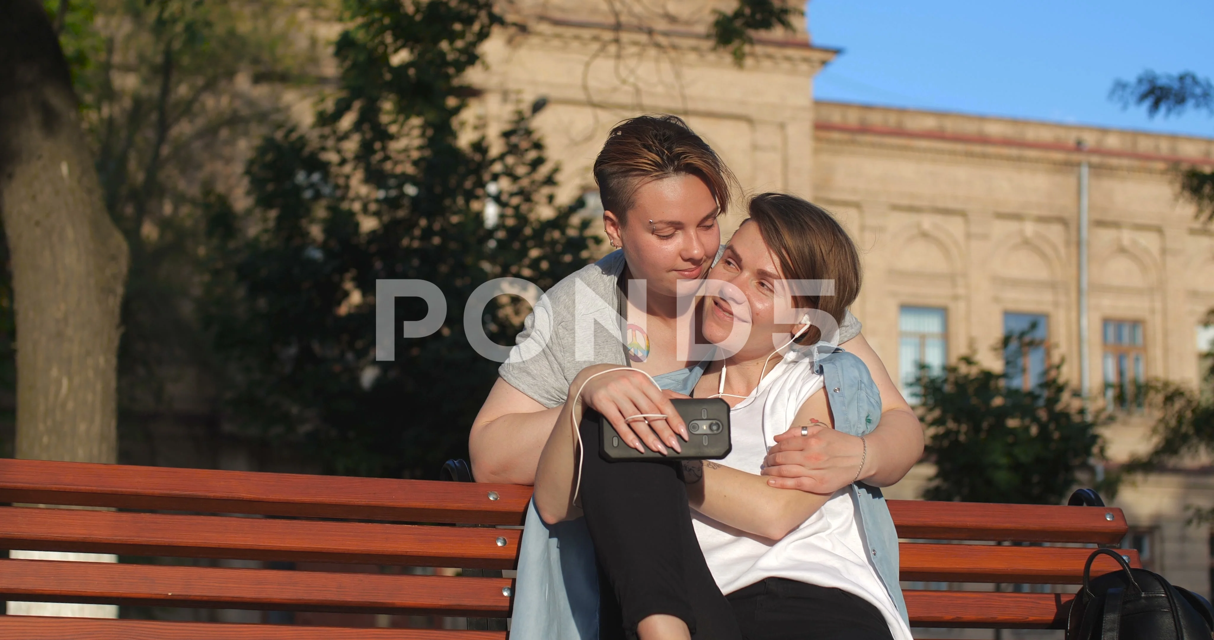 Female same-sex couple sitting on a bench in city park.