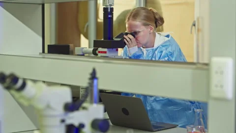 Female scientist analyzing a sample with a microscope and laptop Vídeo Stock 346939731