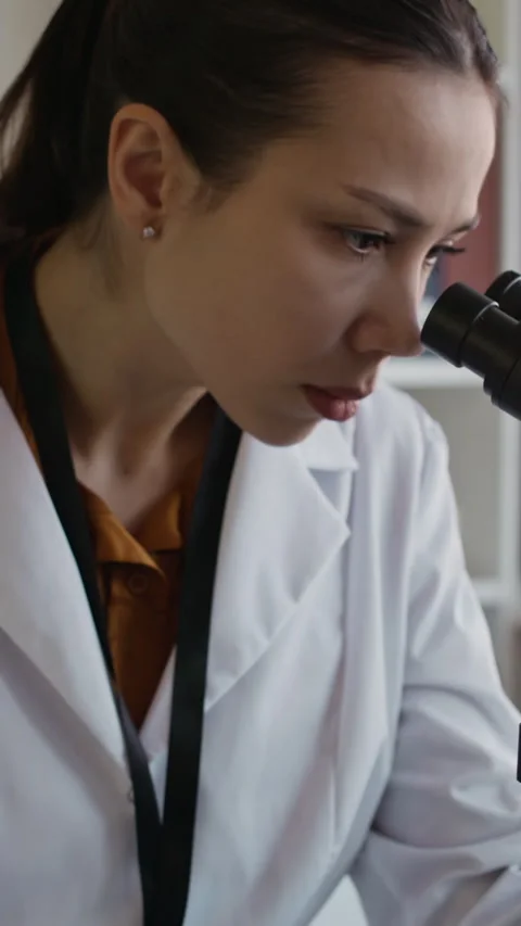 Female Scientist Analyzing Sample under Microscope and Taking Notes in Lab Stock Footage 332358925