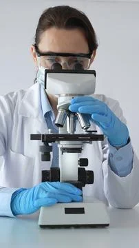 Female scientist examining microscope slide, wearing protective gear in Stock Photos