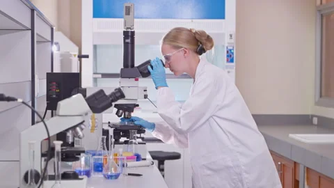 Female scientist examining a sample through a laboratory microscope Vídeos de archivo 346938836