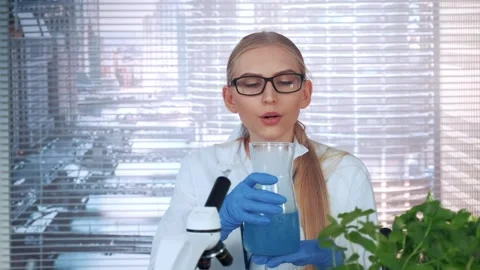 Female scientist explaining blue liquid in conical flask in laboratory Stock Footage 340985484