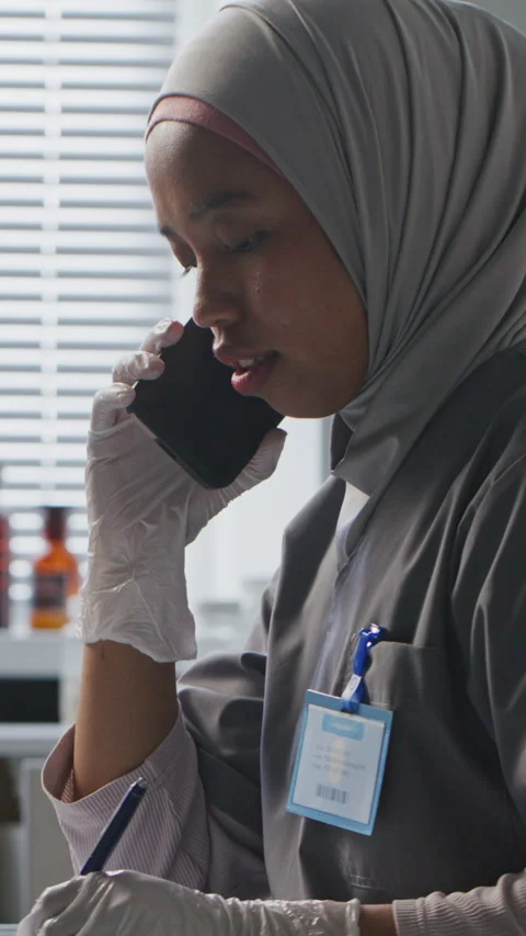 Female Scientist in Hijab Writing Notes during Phone Talk in Laboratory Stock Footage 312473151