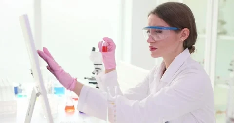 Female scientist holds sample vial comparing tests results in lab Stock Footage 309033552