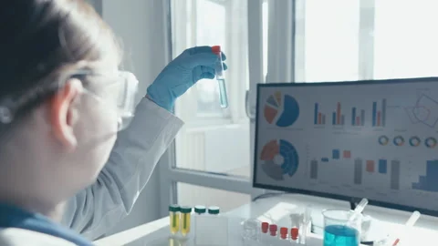 Female scientist in laboratory analyzing blue liquid in test tube while Stock Footage 340926206