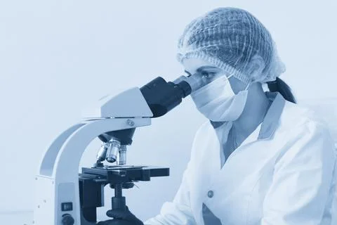 Female scientist looking through microscope in modern chemical laboratory doing Stock Photos