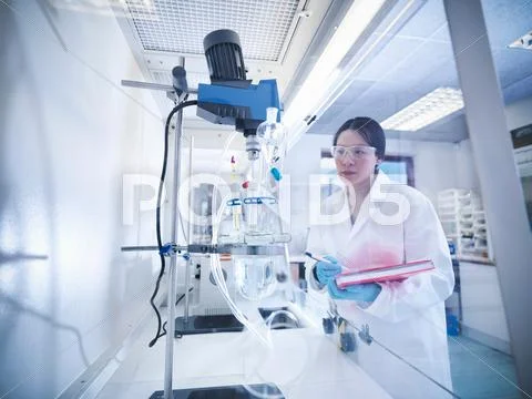 Female Scientist With Notebook Inspecting Equipment In Laboratory