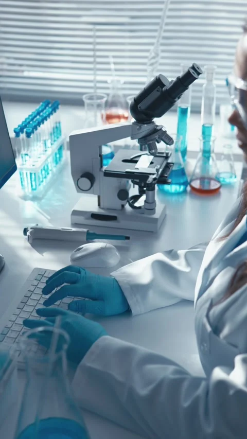 Female scientist in protective gloves and lab coat working on a computer in a Stock Footage 340924656