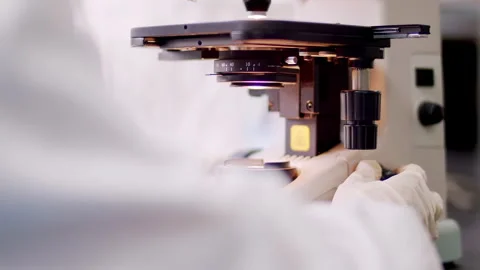 Female scientist in protective suit, goggles, gloves using microscope conduct Stock Footage 346174249