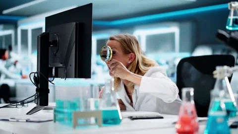 Female Scientist Using Magnifying Glass To Search For Document On Computer Stock Footage 317854252