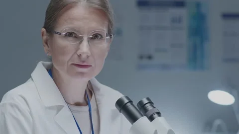 Female Scientist Using Microscope and Looking at Camera Video stock 236422354