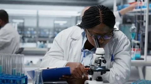 Female scientist using optical microscope to study microorganisms in laboratory Stock Photos