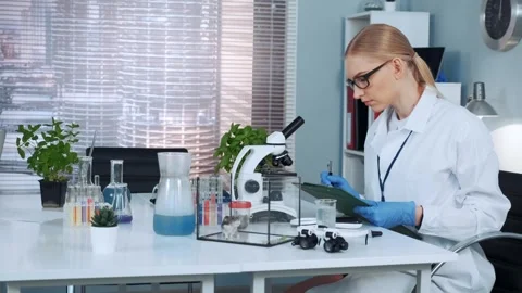 Female scientist writing notes at laboratory table with microscope Stock Footage 340981072