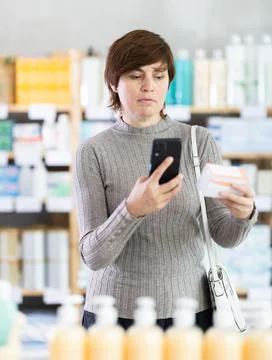 Female shopper in pharmacy scanning barcode on box of pills with smartphone Stock Photos