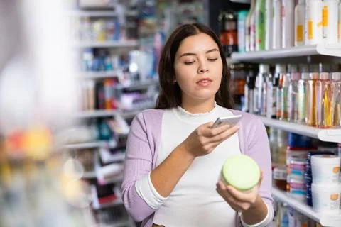 Female shopper scanning a QR code using a mobile phone in cosmetics store Stock Photos