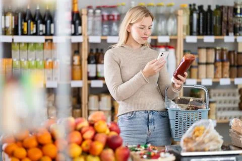 Female shopper scanning QR code on bottle ketchup label in grocery department of Stock Photos