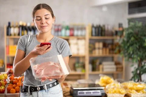 Female shopper scanning QR code on meat label in grocery department of Foto stock