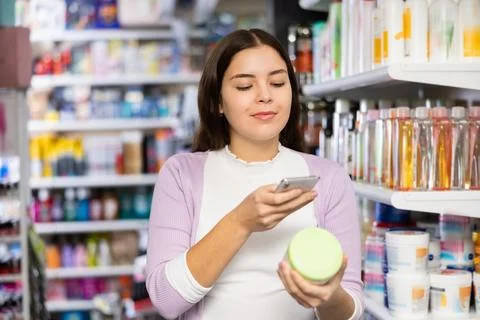 Female shopper scanning a QR code using a mobile phone in cosmetics store Foto stock