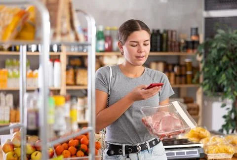 Female shopper scanning QR code on meat label in grocery department of Stock Photos