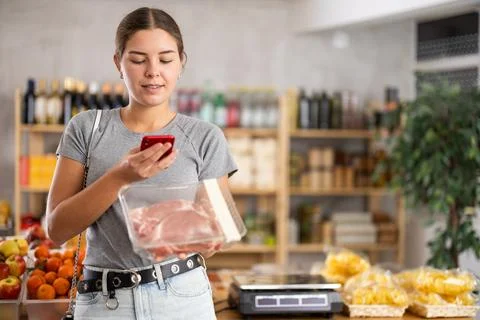 Female shopper scanning QR code on meat label in grocery department of Fotos de archivo
