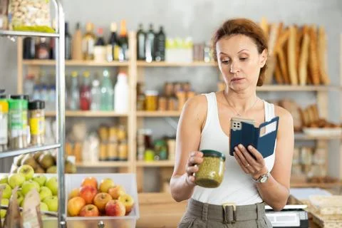 Female shopper scans QR code on green peas jar label using smartphone. Checking Foto stock