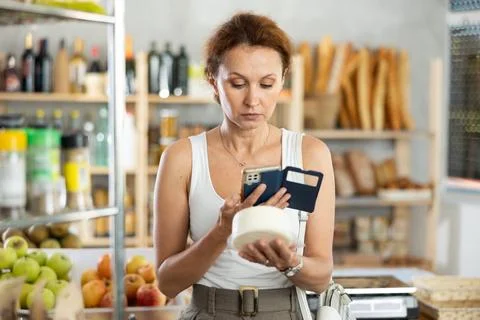 Female shopper scans QR code on cheese label using smartphone. Checking products Stock Photos