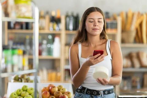 Female shopper scans QR code on cheese label using smartphone. Checking products Stock Photos