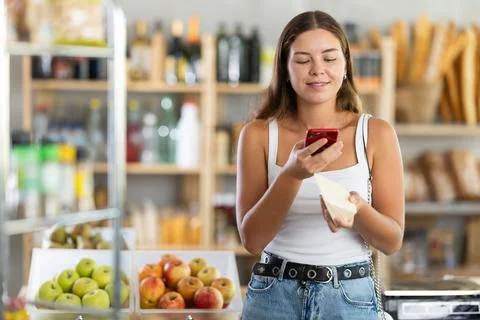 Female shopper scans QR code on cheese label using smartphone. Checking products 스톡 사진