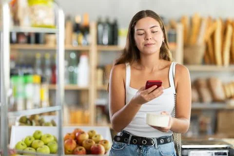 Female shopper scans QR code on cheese label using smartphone. Checking products Foto stock