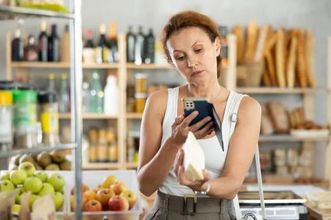Female shopper scans QR code on cheese label using smartphone. Checking products Stock Photos