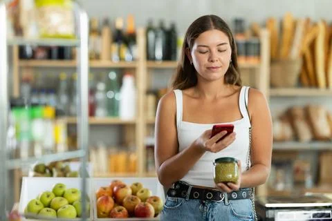 Female shopper scans QR code on green peas jar label using smartphone. Checking Stock Photos
