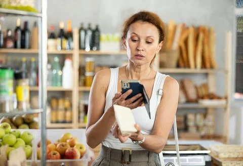 Female shopper scans QR code on cheese label using smartphone. Checking products Stock Photos