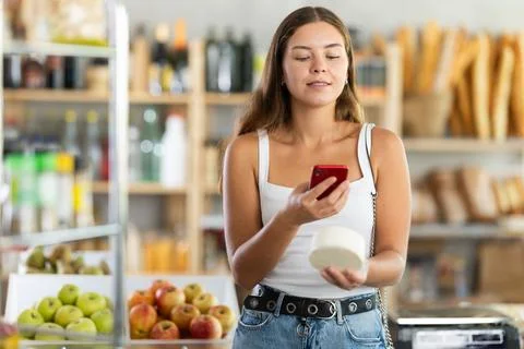 Female shopper scans QR code on cheese label using smartphone. Checking 写真素材
