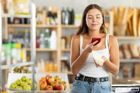 Female shopper scans QR code on cheese label using smartphone. Checking 스톡 사진