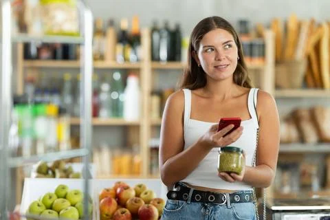 Female shopper scans QR code on green peas jar label using smartphone. Checking 写真素材
