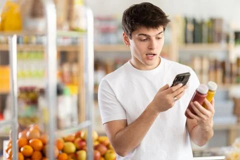 Female shopper scans QR code on bottle of smoothie with her smartphone 스톡 사진