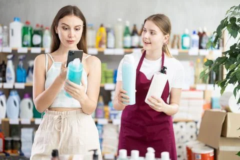 Female shopper scans QR code on label of shampoo using her smartphone. Young Foto stock